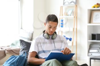 African-American teenage boy reading book at home�
