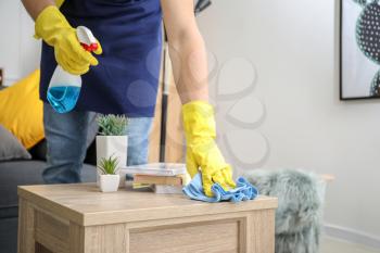 Male janitor cleaning table in room�