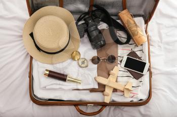 Suitcase with female clothes and travel accessories on bed�