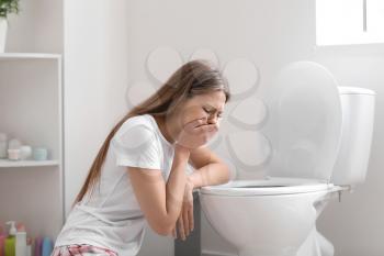 Pregnant woman suffering from toxicosis near toilet bowl in bathroom�