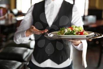 Young female waiter with salad in restaurant, closeup�