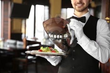 Young male waiter with salad in restaurant�