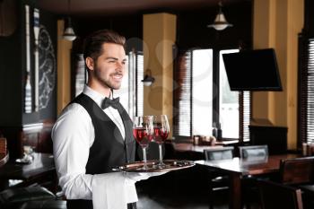 Young male waiter with glasses of wine in restaurant�