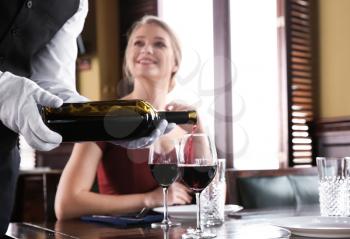 Waiter pouring wine in glasses for clients in restaurant�