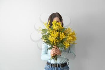 Young woman holding bouquet of beautiful mimosa flowers on light background�