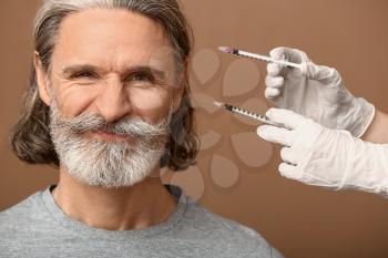 Mature man and hands holding syringes for anti-aging injections on color background 