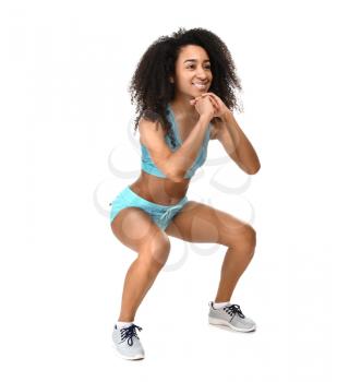 Sporty African-American woman doing squats on white background�