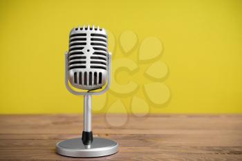 Retro microphone on table against color background�