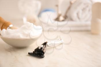 Razor and bowl with shaving foam on table�