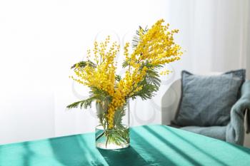 Vase with beautiful mimosa flowers on table in room�