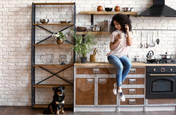 African-American woman with cute funny dog drinking coffee in kitchen�