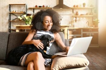 Beautiful African-American woman with cute dog working on laptop at home�