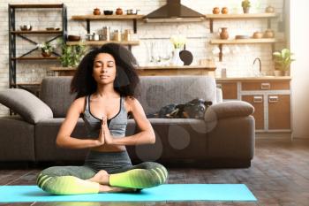 Sporty African-American woman practicing yoga at home�