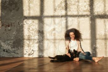 Beautiful African-American woman with cute dog sitting on floor near grunge wall�