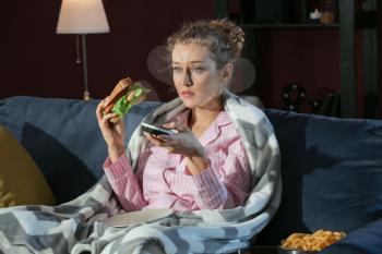 Beautiful young woman eating unhealthy food while watching TV at night�