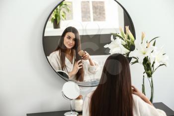Beautiful young woman combing her healthy long hair near mirror at home�