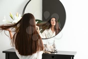 Beautiful young woman with healthy long hair looking in mirror at home�