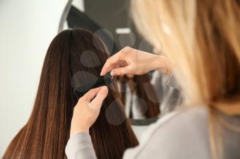 Hairdresser combing long hair of young woman in salon�