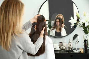 Hairdresser working with long hair of young woman in salon�