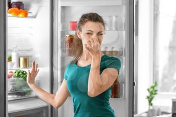 Young woman feeling bad smell from refrigerator in kitchen�