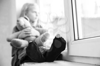 Homeless little girl sitting on window sill�