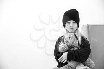 Homeless little girl with teddy bear indoors�