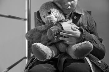 Homeless little boy with teddy bear sitting indoors�