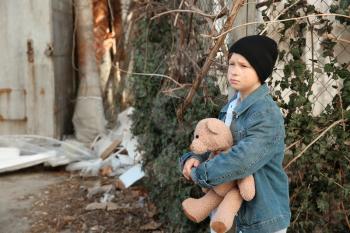 Homeless little boy with teddy bear outdoors�