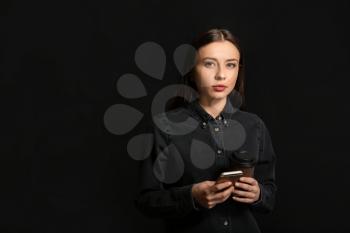 Stylish businesswoman with cup of coffee and mobile phone on dark background�