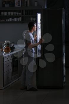 Handsome young man choosing food in refrigerator at night�
