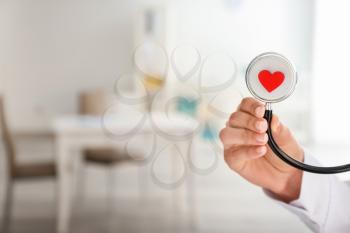 Cardiologist holding stethoscope with red heart in clinic, closeup�