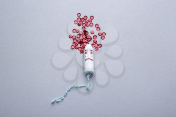 Tampon and red sequins on light background. Menstruation concept�