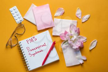 Composition with menstrual pads, notebook with text PMS, PREMENSTRUAL SYNDROME, flower and pills on color background�