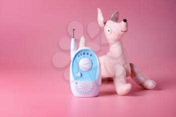 Modern baby monitor with toy on color background�