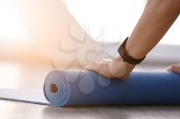 Young woman rolling out yoga mat in gym, closeup�