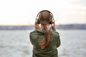 Young woman listening to music near river�