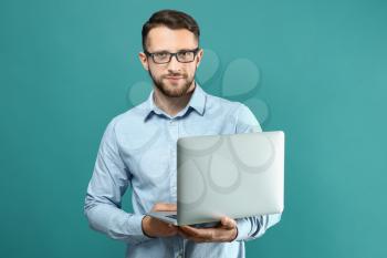 Handsome man with laptop on color background�