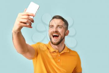 Handsome man taking selfie on color background�