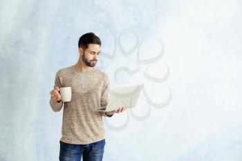 Male programmer with laptop and cup of coffee on color background�