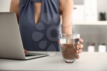 Woman drinking water while working on laptop in office�