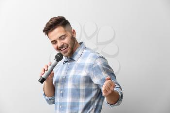 Handsome male singer with microphone on light background�