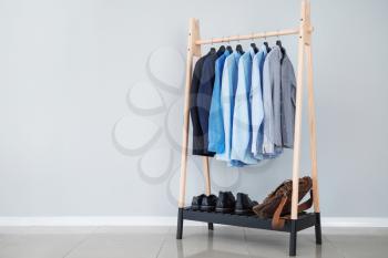 Rack with stylish male clothes near light wall�
