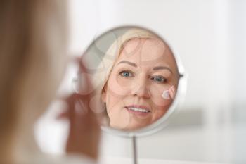 Mature woman applying facial cream at home�
