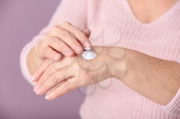 Mature woman applying hand cream on color background, closeup�