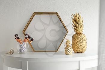 Golden pineapples with makeup brushes and mirror on table near white wall�