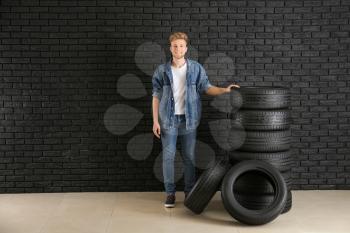 Young man with car tires against dark wall�