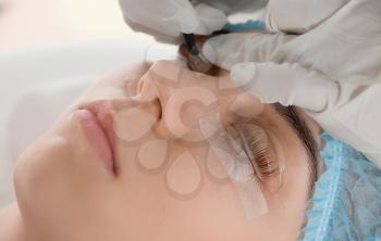 Young woman undergoing procedure of eyelashes lamination in beauty salon, closeup�