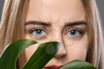 Beautiful young woman with laminated eyelashes and tropical leaf, closeup�
