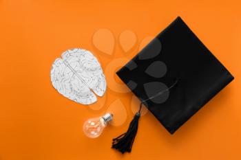 Mortar board with paper brain and light bulb on color background. Concept of high school graduation�