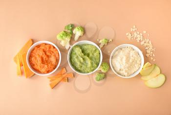Bowls with healthy baby food on color background�